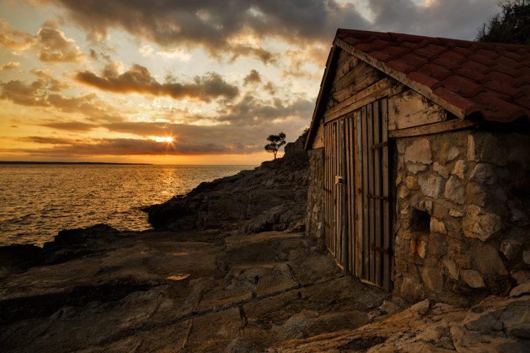 Sunrise over a boathouse on Osiri Beach on the coastal area of Cunski, which lies just 8kms north of Mali Losinj on Losinj Island, Croatia. The strip of land to the left is Punta Kriza.