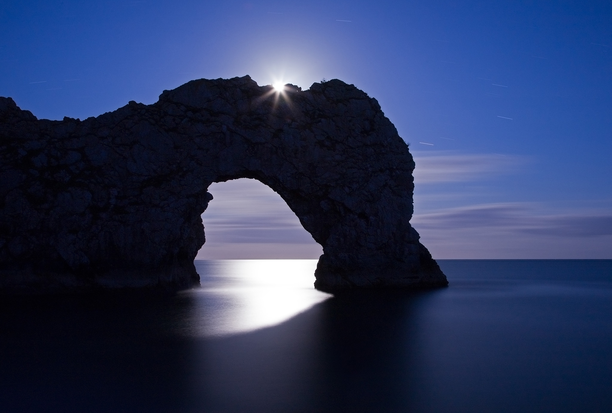 Durdle Door in the moonlight, Dorset, England. Captured late evening as the moonlight flooded through the rock's archway. The long exposure has also produced some nice star trails to the right of the arch. Durdle door is one of the many stunning locations to visit on the Jurassic coast in southern England.