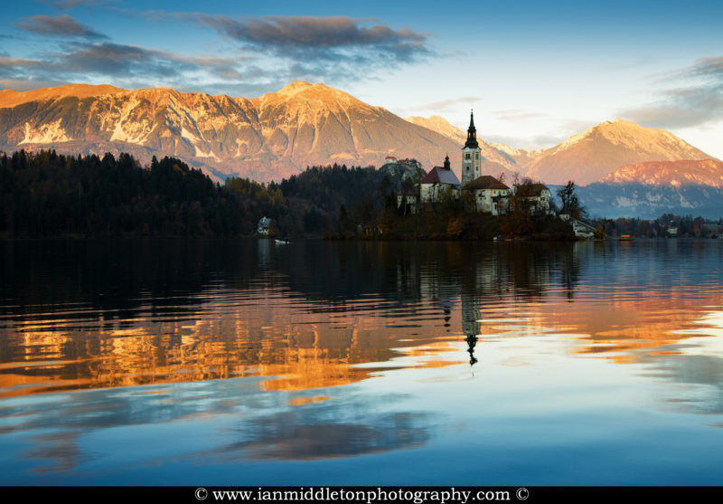 View across the beautiful Lake Bled, island church and hilltop castle at sunset with the beautiful Karawanke mountains in the background, Slovenia. Lake Bled is Slovenia's most popular tourist destination and the Karawanke mountains form the border between Slovenia and Austria.