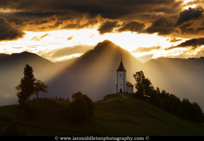 Jamnik church of Saints Primus and Felician at sunrise, perched on a hill on the Jelovica Plateau with the kamnik alps and storzic mountain in the background, Slovenia.
