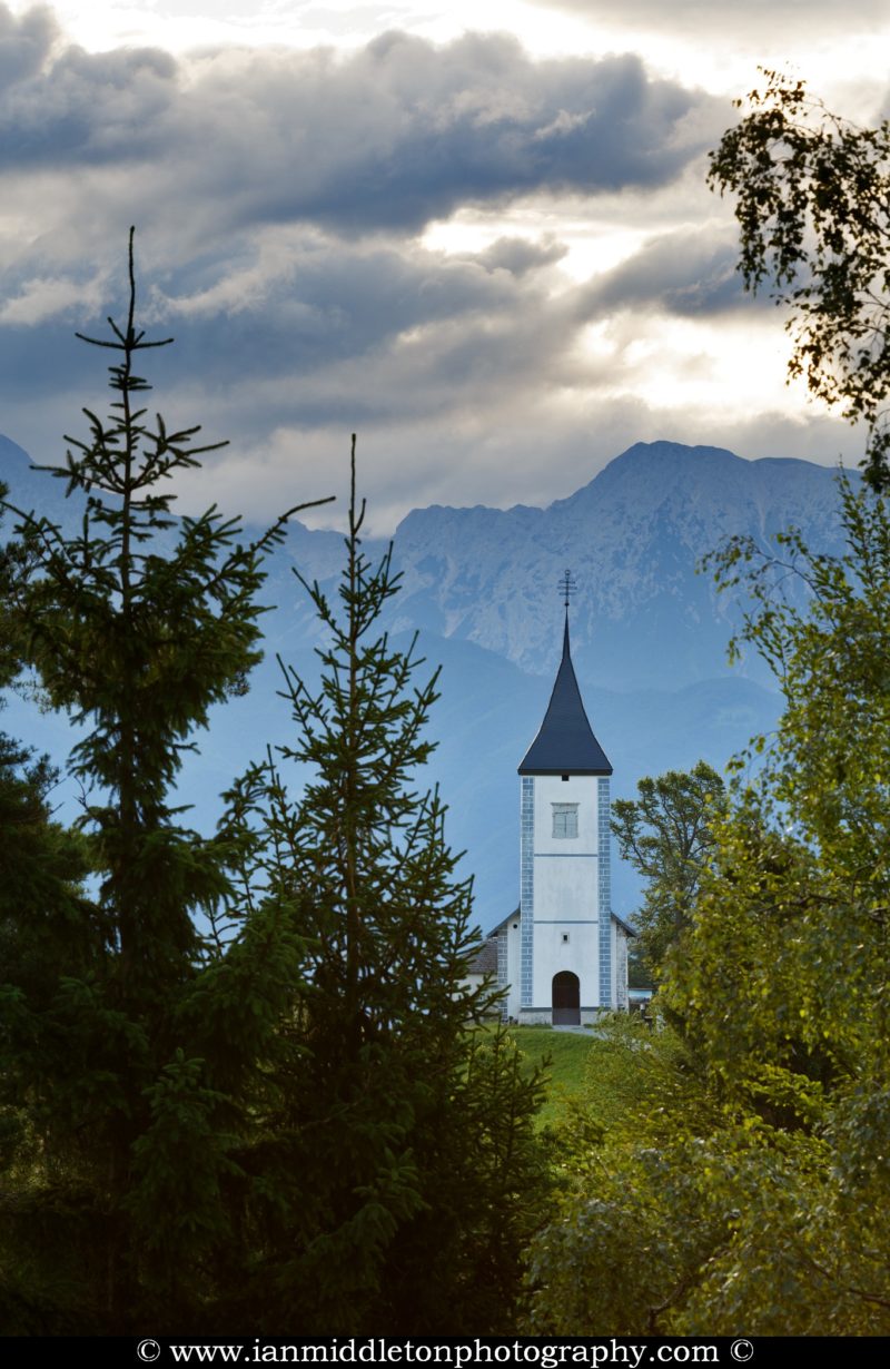 Jamnik church of Saints Primus and Felician, perched on a hill on the Jelovica Plateau with the kamnik alps and Storzic mountain in the background, Slovenia.