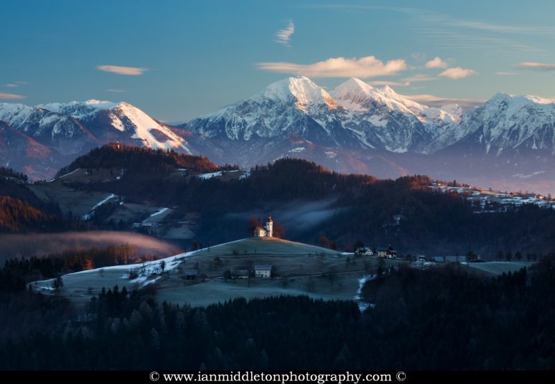 View at sunrise in winter from Rantovše hill across to Sveti Tomaz nad Praprotnim (church of Saint Thomas) and the Kamnik Alps, Slovenia.