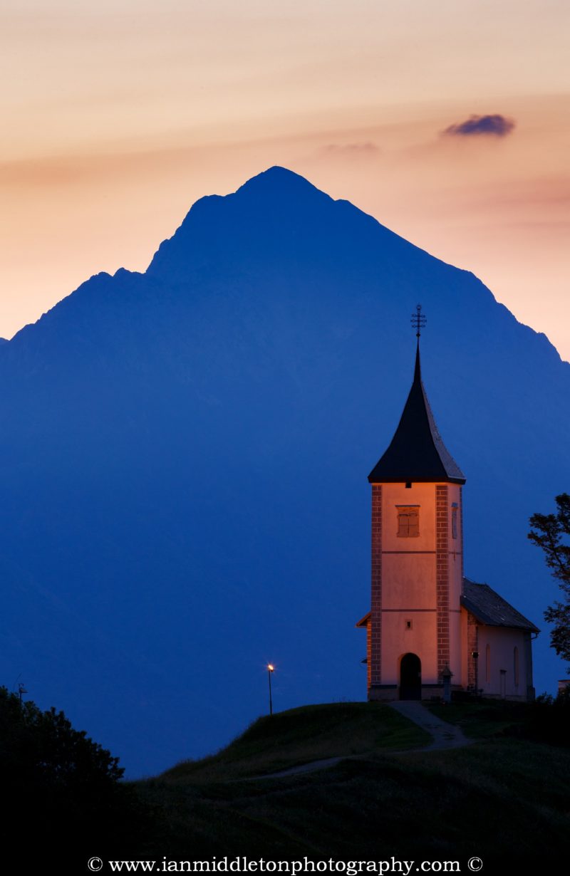Jamnik church of Saints Primus and Felician, perched on a hill on the Jelovica Plateau with the kamnik alps and storzic mountain in the background, Slovenia.