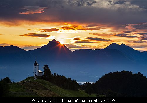 Jamnik church of Saints Primus and Felician at sunrise, perched on a hill on the Jelovica Plateau with the kamnik alps and storzic mountain in the background, Slovenia.