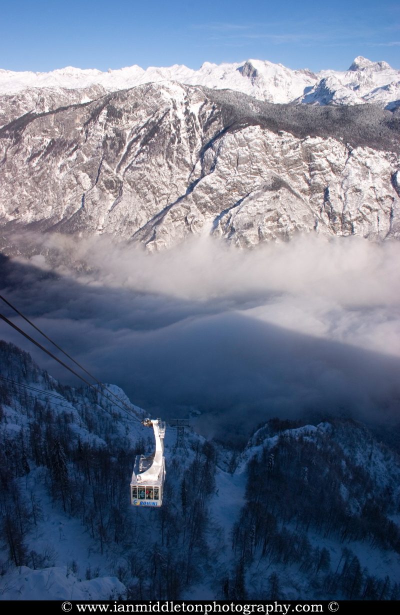 Winter view from Vogel Mountain as the cable car brings skiers up to the mountain, Slovenia. In the background you can see the snow covered Julian Alps and their highest mountain, Mount Triglav, covered in snow. The morning mist fills the valley.