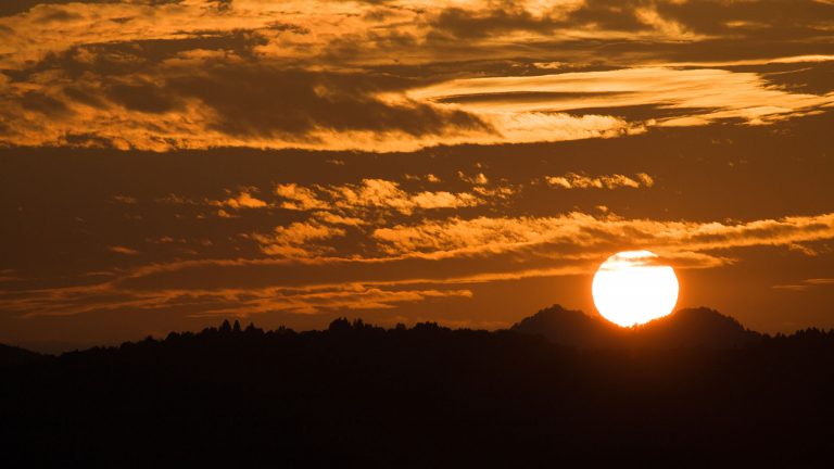 Sun setting between two mountain peaks to the west of Ljubljana, Slovenia.