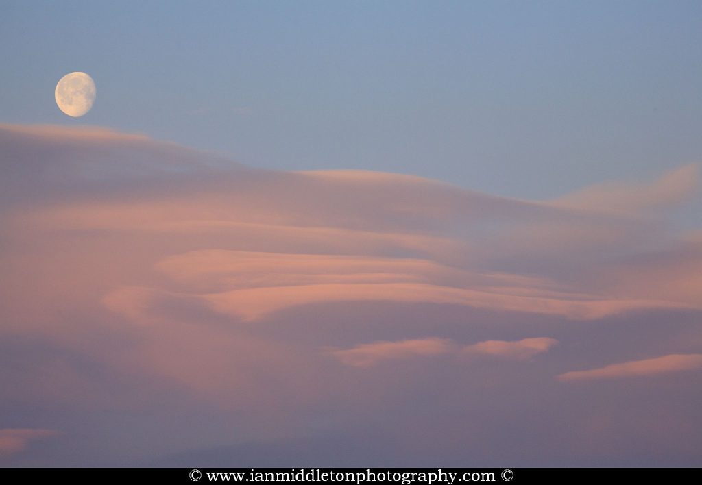 Lenticular cloud formation (Altocumulus lenticularis) at sunrise with the waning moon setting above then over residential area of Ljubljana taken from a sixth floor apartment , Slovenia