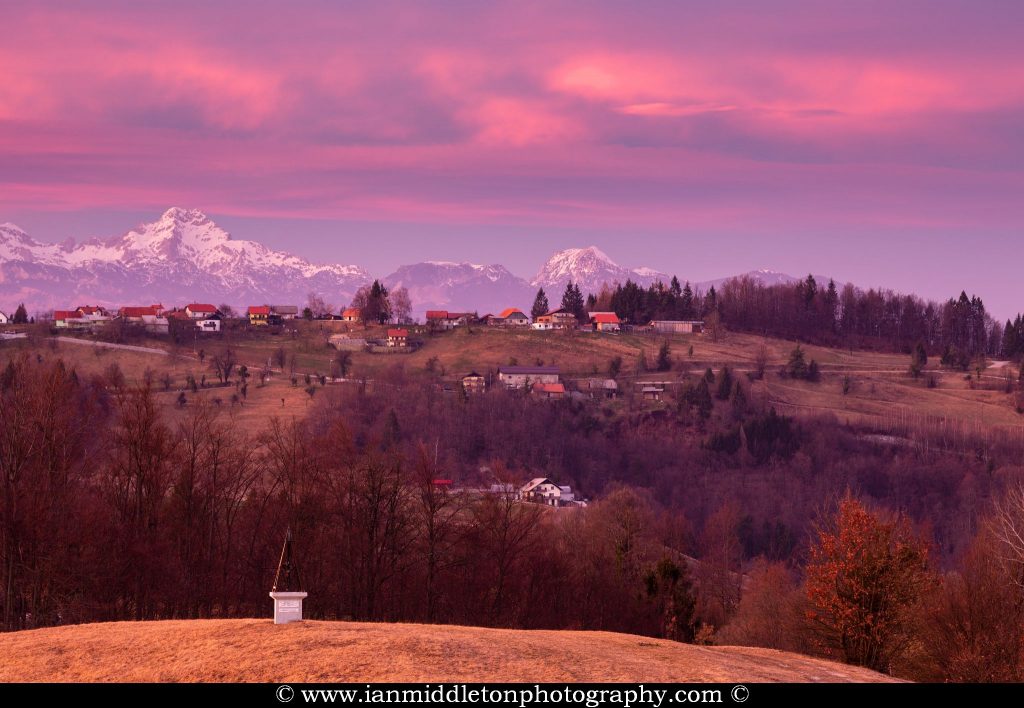 Sunset view across a hill in prezganje to the Kamnik Alps. The shrine on the first hill is to Jesus Christ, built to commemorate the first visit of Pope John Paul the second to Slovenia in 1996.