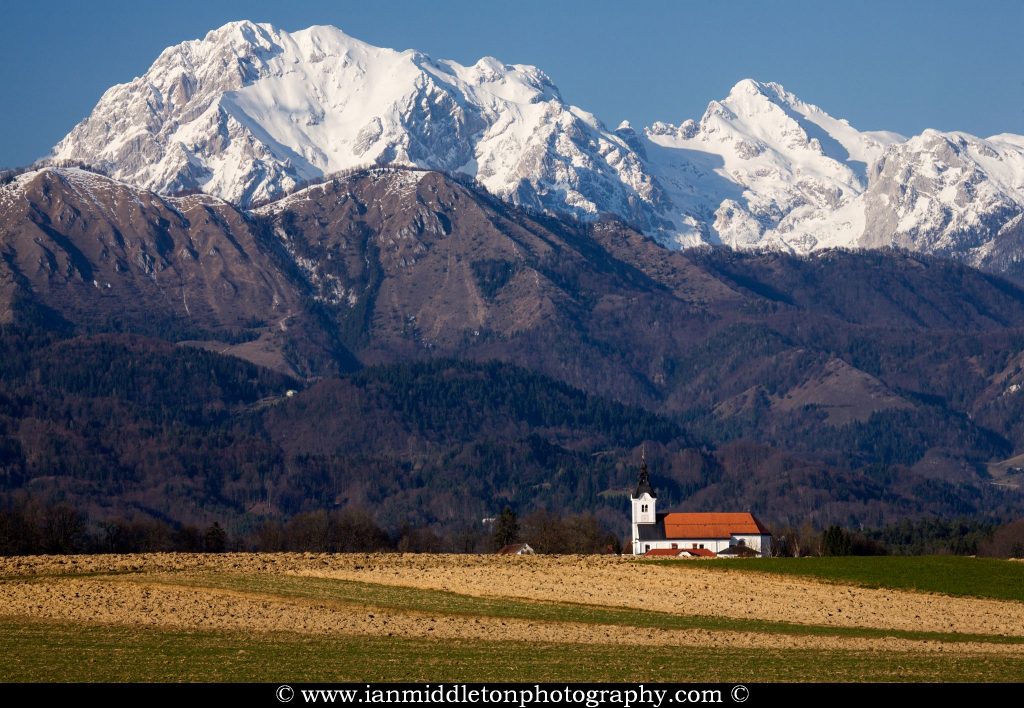 Mountaintops of the Kamnik Alps with the church of Saint Peter sitting in its shadow. This complex also contains a castle, a baroque church, a parsonage, a cemetery and a fairly large stable. The Alps have a fresh coating of snow after an abundance of snow this winter