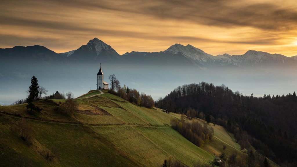 Jamnik church of Saints Primus and Felician at sunrise, perched on a hill on the Jelovica Plateau with the kamnik alps and storzic mountain in the background, Slovenia.