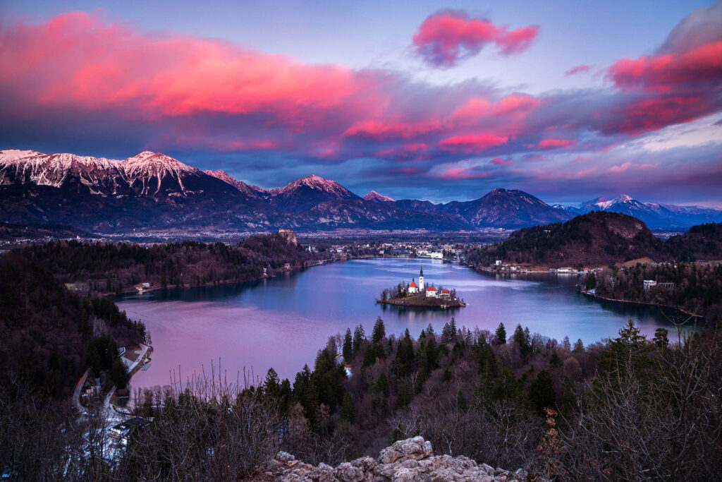 View across Lake Bled to the island church and clifftop castle from Ojstrica at sunset, Slovenia.