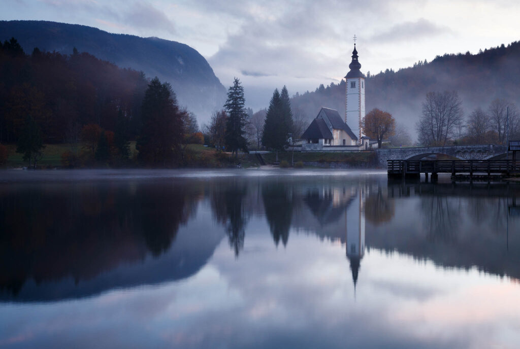 Morning mist and cloud over Lake Bohinj and the Church of Saint John at sunrise, Triglav National Park, Slovenia