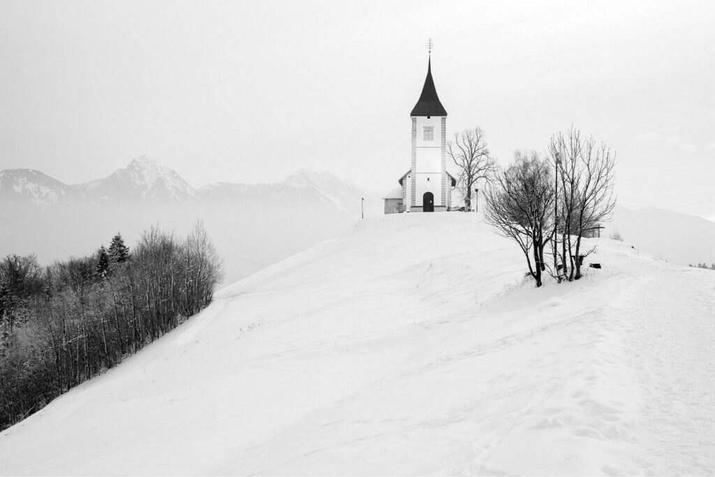 Jamnik church of Saints Primus and Felician, perched on a hill on the Jelovica Plateau with the kamnik alps and Storzic mountain in the background, Slovenia.