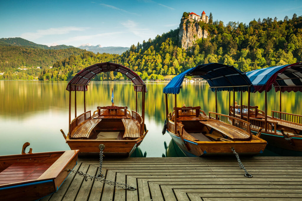 Beautiful morning light across the beautiful Lake Bled and the hilltop castle with the Julian Alps beside it and Pletna boats in moored beside the lake. Slovenia.