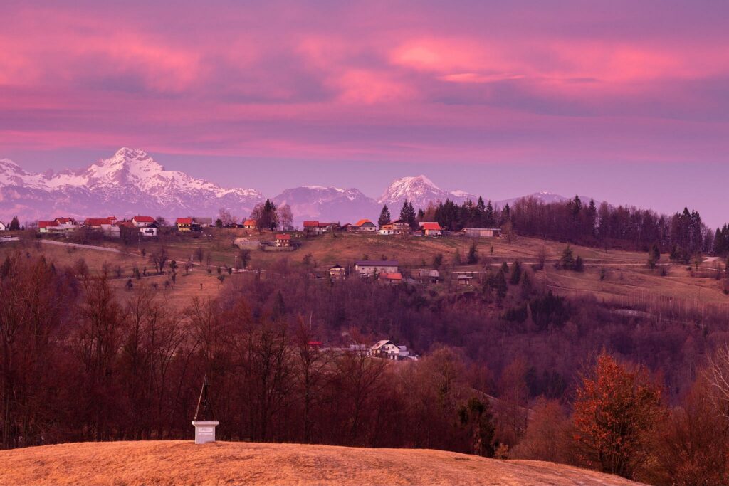 Sunset view across a hill in prezganje to the Kamnik Alps. The shrine on the first hill is to Jesus Christ, built to commemorate the first visit of Pope John Paul the second to Slovenia in 1996.