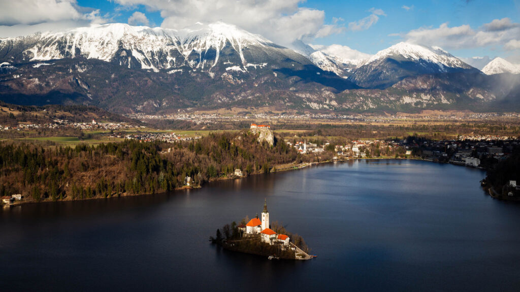 View across Lake Bled to the island church and clifftop castle from Mala Osojnica in spring, Slovenia.