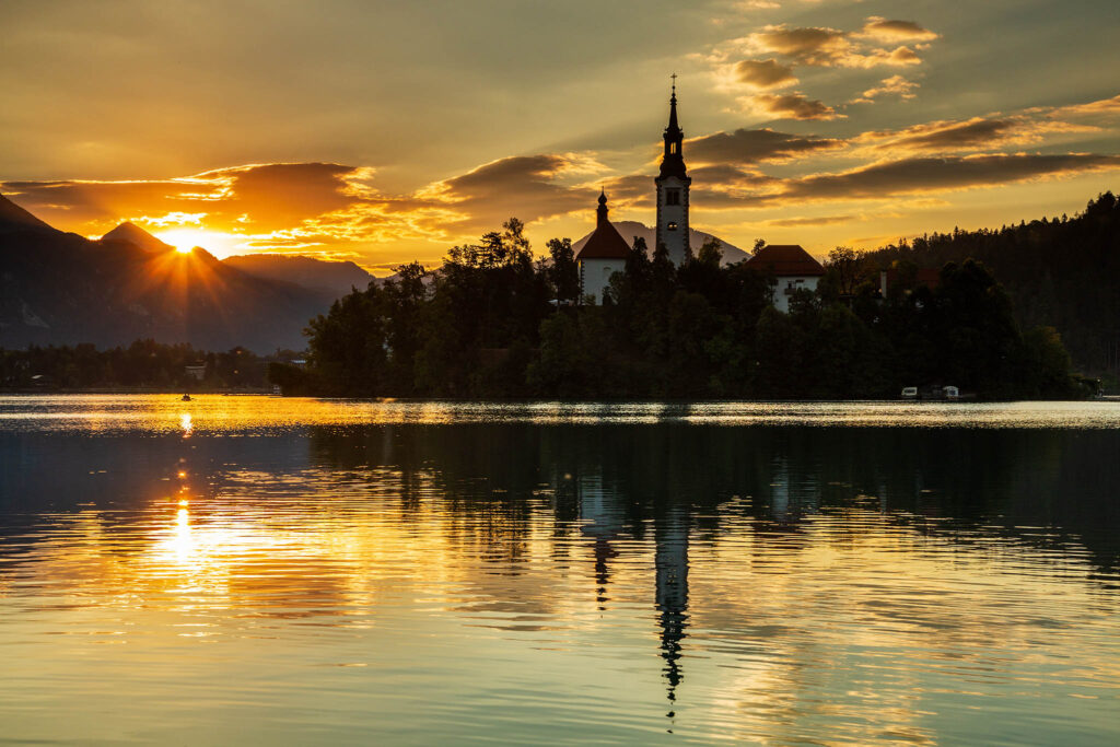 Sun rising over Lake Bled and the island church of the assumption of Mary with the Karavanke mountains in the background, Slovenia.