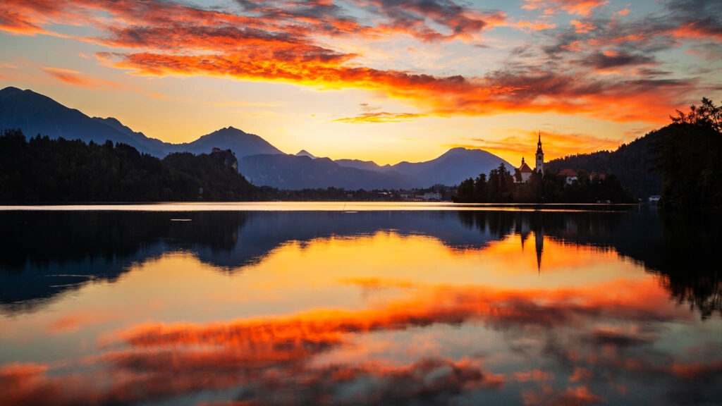 Sun rising over Lake Bled and the island church of the assumption of Mary with the Karavanke mountains in the background, Slovenia.