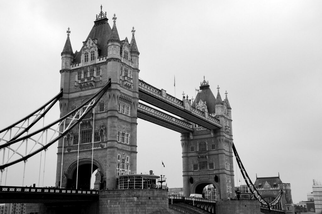 Black and white photo of Tower Bridge in London, England. This is a a combined bascule and suspension bridge, close to the tower of London and crosses the River Thames. It has become a distinctive landmark of the city.