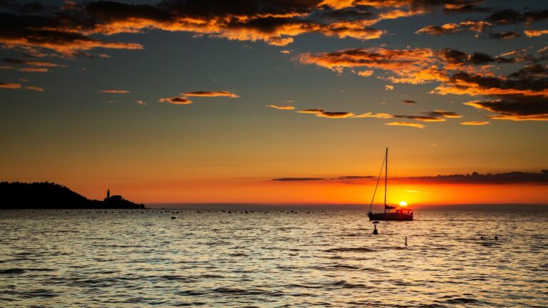 Sun setting over the Adriatic Sea with the Church of Saint George in Piran and a boat sailing by, Slovenia