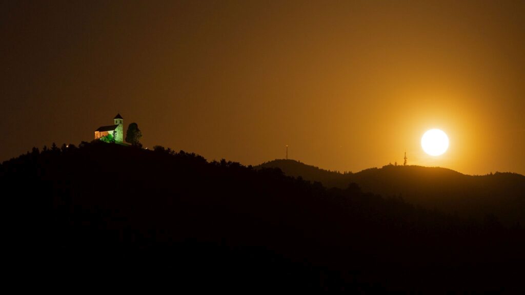 The June 24th 2021 supermoon (strawberry moon) rising beside the Church of Saint Ana and Mount Krim on the Ljubljana Moors in Slovenia.