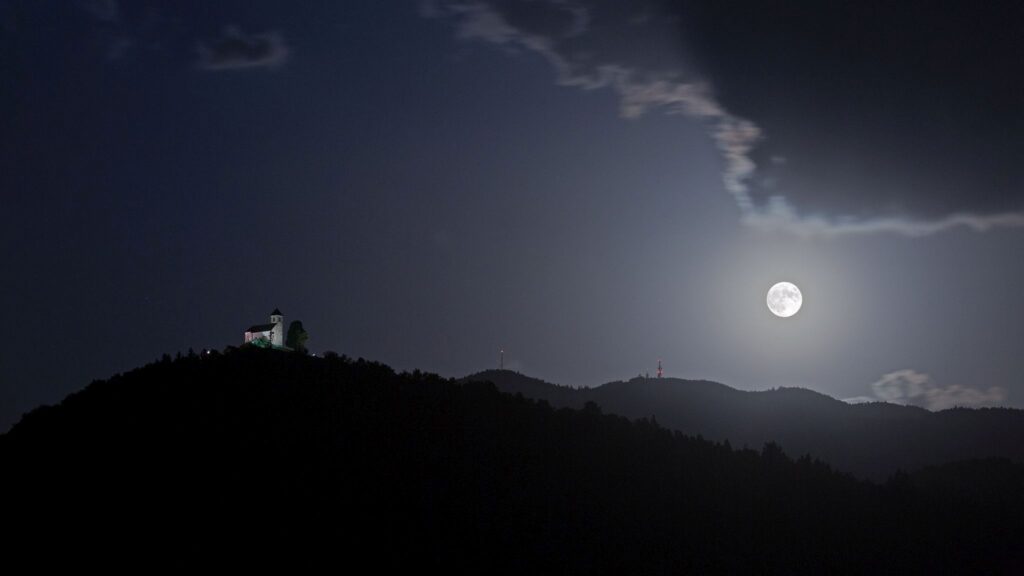 The June 2021 supermoon rising beside the Church of Saint Ana and Mount Krim on the Ljubljana Moors in Slovenia.