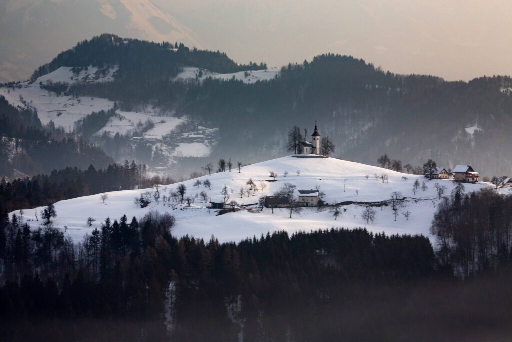 View at sunrise in winter from Rantovše hill across to Sveti Tomaz nad Praprotnim (church of Saint Thomas) and the Kamnik Alps, Slovenia.