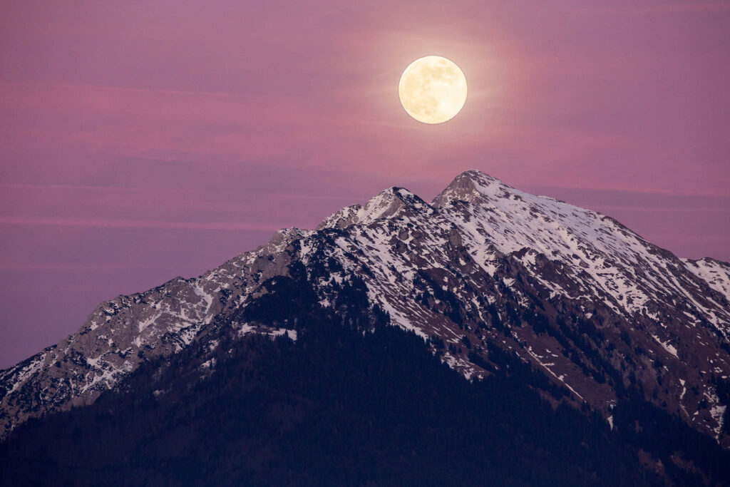 Full moon rising over Veliki Vrh at sunset, part of the Karavanke Alps in Slovenia.