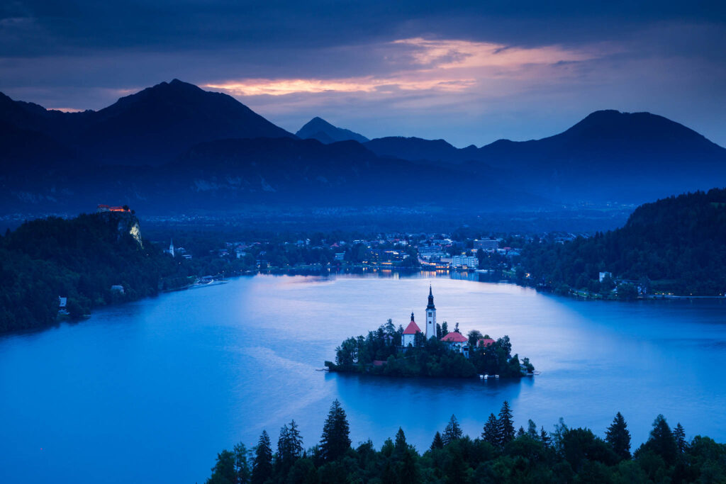 View across Lake Bled to the island church and clifftop castle from Ojstrica, Slovenia.