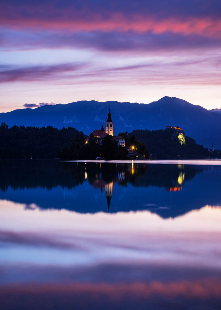 View across the beautiful Lake Bled, island church of the assumption of Mary, and hilltop castle at dawn, Slovenia.