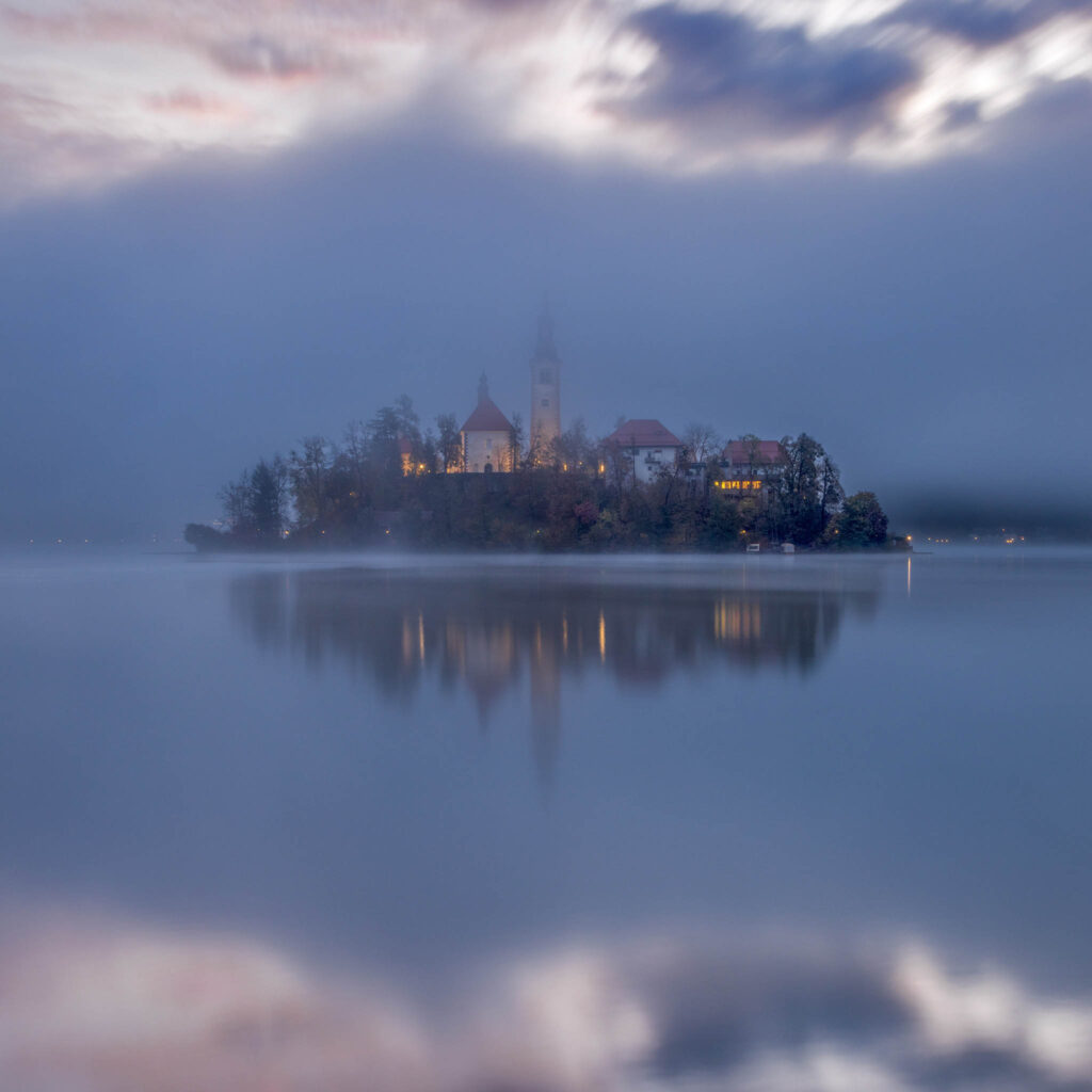 View across the beautiful Lake Bled, island church of the assumption of Mary in the mist at dawn, Slovenia.