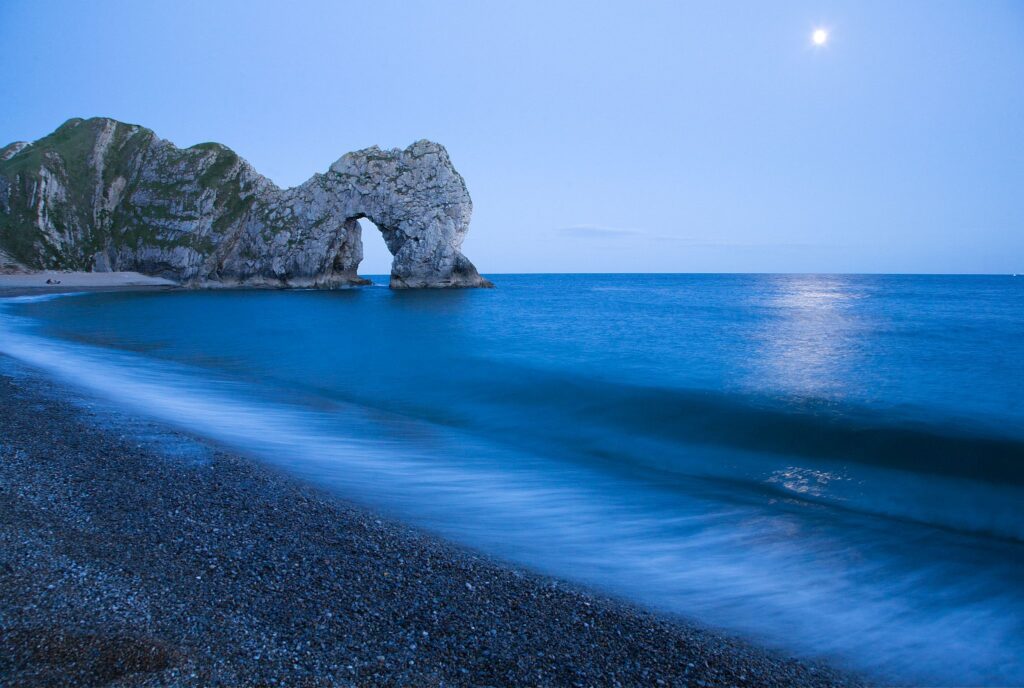 Durdle Door and beach in the moonlight, Dorset, England. Captured late evening as the moonlight flooded across the sea. Durdle door is one of the many stunning locations to visit on the Jurassic coast in southern England.