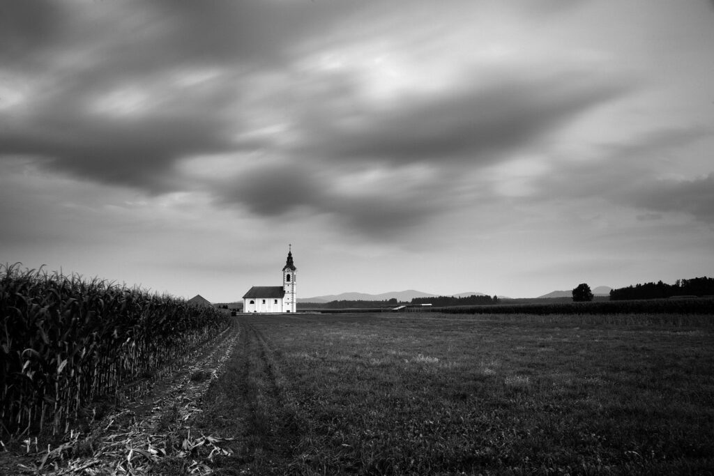 Black and white version of View of the the church of saint John (Sveti Janez) at dusk as storm clouds drift over, Brnik, Slovenia.