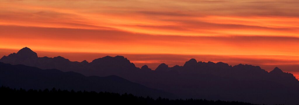 Panoramic view of the sun setting behind the Julian Alps mountains of Slovenia. This image is a 2 frame panoramic taken from a field in Brnik near Ljubljana Airport.