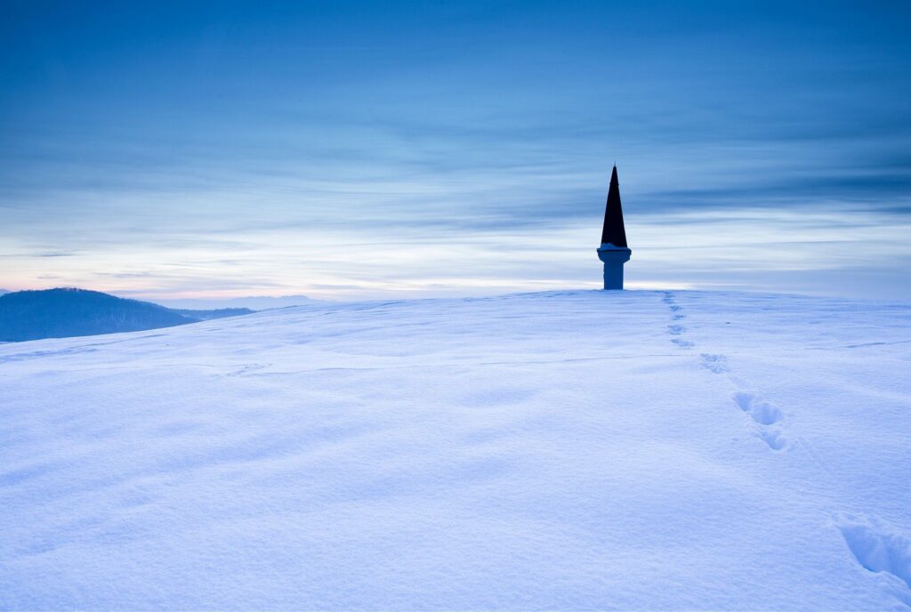 Twilight winter view across a hill in prezganje in the Jance hills to the east of Ljubljana, Slovenia. Footprints are leading up to a shrine. The shrine is to Jesus Christ, built to commemorate the first visit of Pope John Paul the second to Slovenia in 1996.