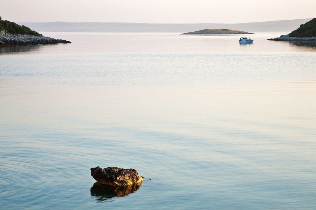 The morning sun casts a soft pink hue over Mali Osir island, seen from Zaosiri Beach on the coast area of Cunski, which lies just 8kms north of Mali Losinj on Losinj Island, Croatia.