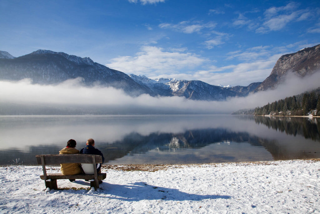 Couple sitting beside Lake Bohinj as the sun burns away the morning mist on New Years Day 2012, Triglav National Park , Slovenia