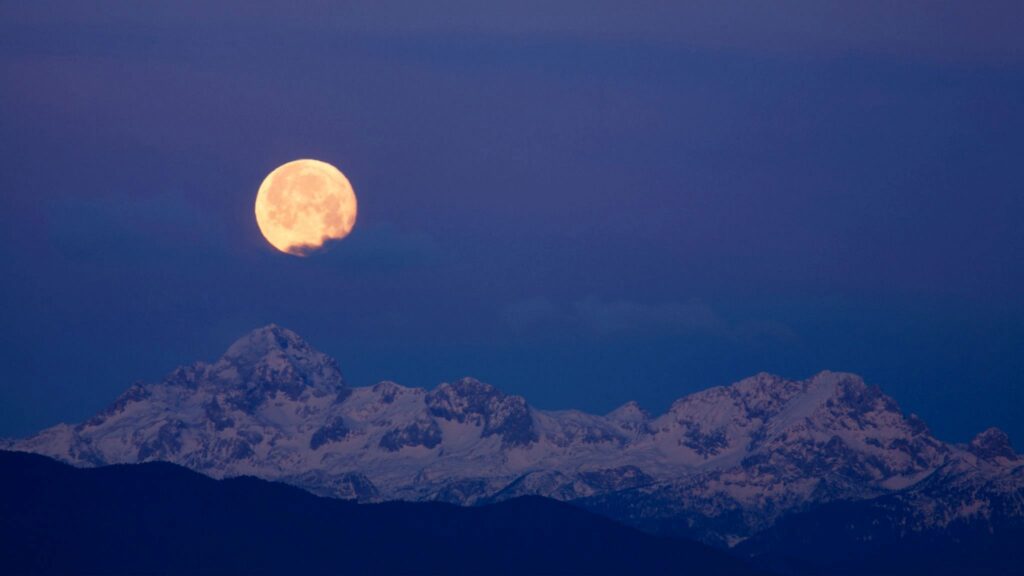 Full moon setting over Mount Triglav, the highest mountain in the Julian Alps at dawn in Slovenia.