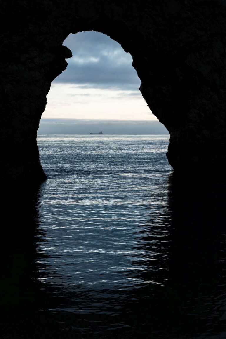 A view through the Durdle Door arch as a cargo ship sails by in the distance, Dorset, England. Durdle door is one of the many stunning locations to visit on the Jurassic coast in southern England.