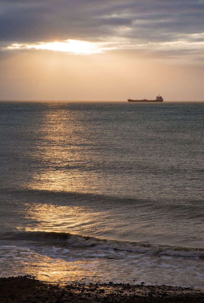 View out to sea in the morning from Kingsdown beach, near the famous White Cliffs of Dover, Kent, England. A cargo ship is anchored in the distance.