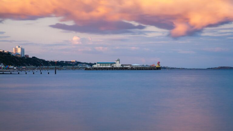 Bournemouth Pier and seafront as a storm cloud drifts over as is illuminated pink by the sunset. Highcliffe can also be seen on the far right.