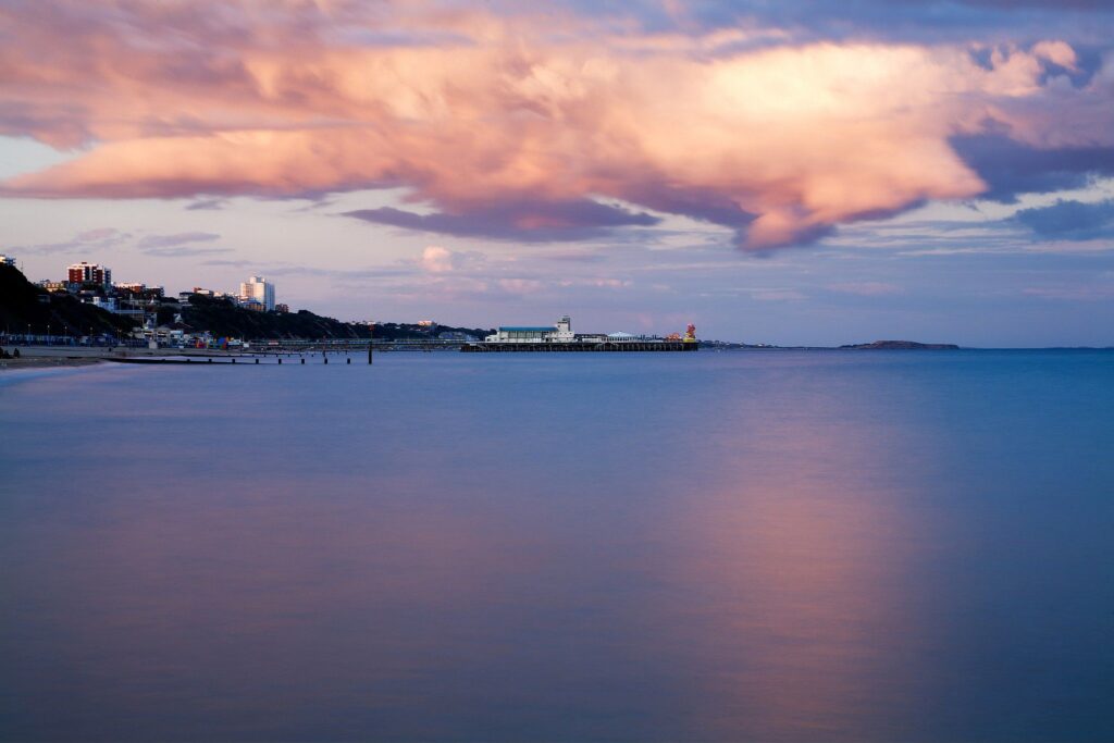 Bournemouth Pier and seafront as a storm cloud drifts over as is illuminated pink by the sunset. Highcliffe can also be seen on the far right.