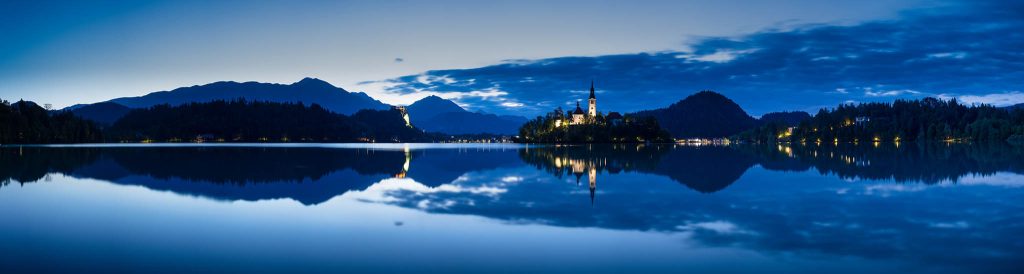 Panoramic view across the beautiful Lake Bled, island church of the assumption of Mary, and hilltop castle at dawn, Slovenia.