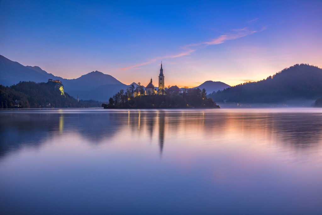 Sun rising over Lake Bled and the island church of the assumption of Mary with the Karavanke mountains in the background, Slovenia.