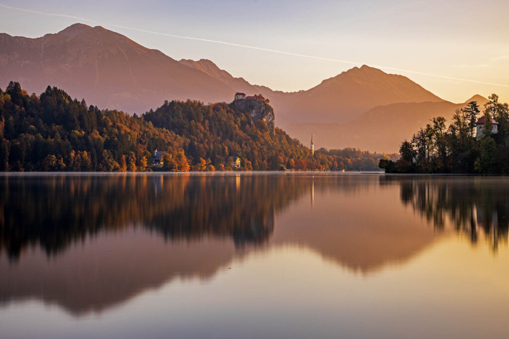 Lake Bled castle and church of Saint Martin with the Karavanke Alps behind during some soft morning autumn light, Slovenia.