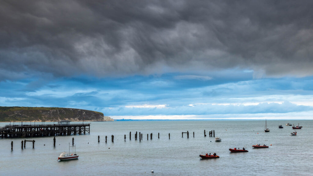 Storm over the old pier in Swanage with Old Harry Cliffs in the background, Dorset, England.