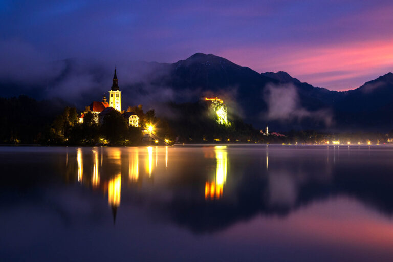 First colour of sunrise over Lake Bled island church of the assumption of Mary, medieval castle and Saint Martin's Church with the Karavanke mountains in the background, Slovenia.