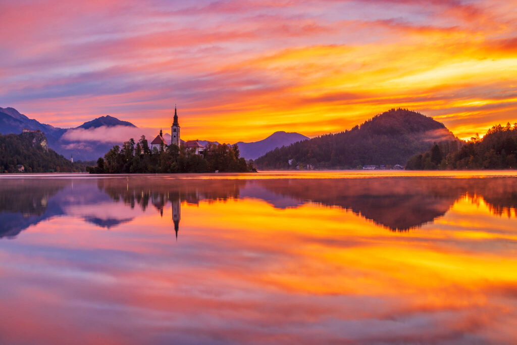 Autumn sunrise over Lake Bled and the island church of the assumption of Mary with the Karavanke mountains in the background, Slovenia.