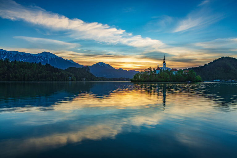 Sunrise over Lake Bled and the island church of the assumption of Mary, castle with the Karavanke mountains in the background, Slovenia.