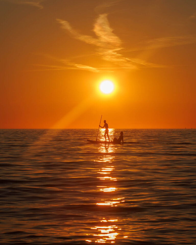 Couple paddling on SUP in the half moon bay at Strunjan on the Adriatic Coast at sunset in Slovenia.